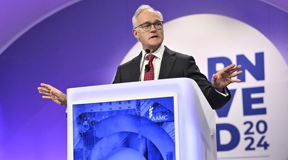 Scott Pelley speaks from behind a podium, with the Learn Serve Lead 2024 backdrop behind him